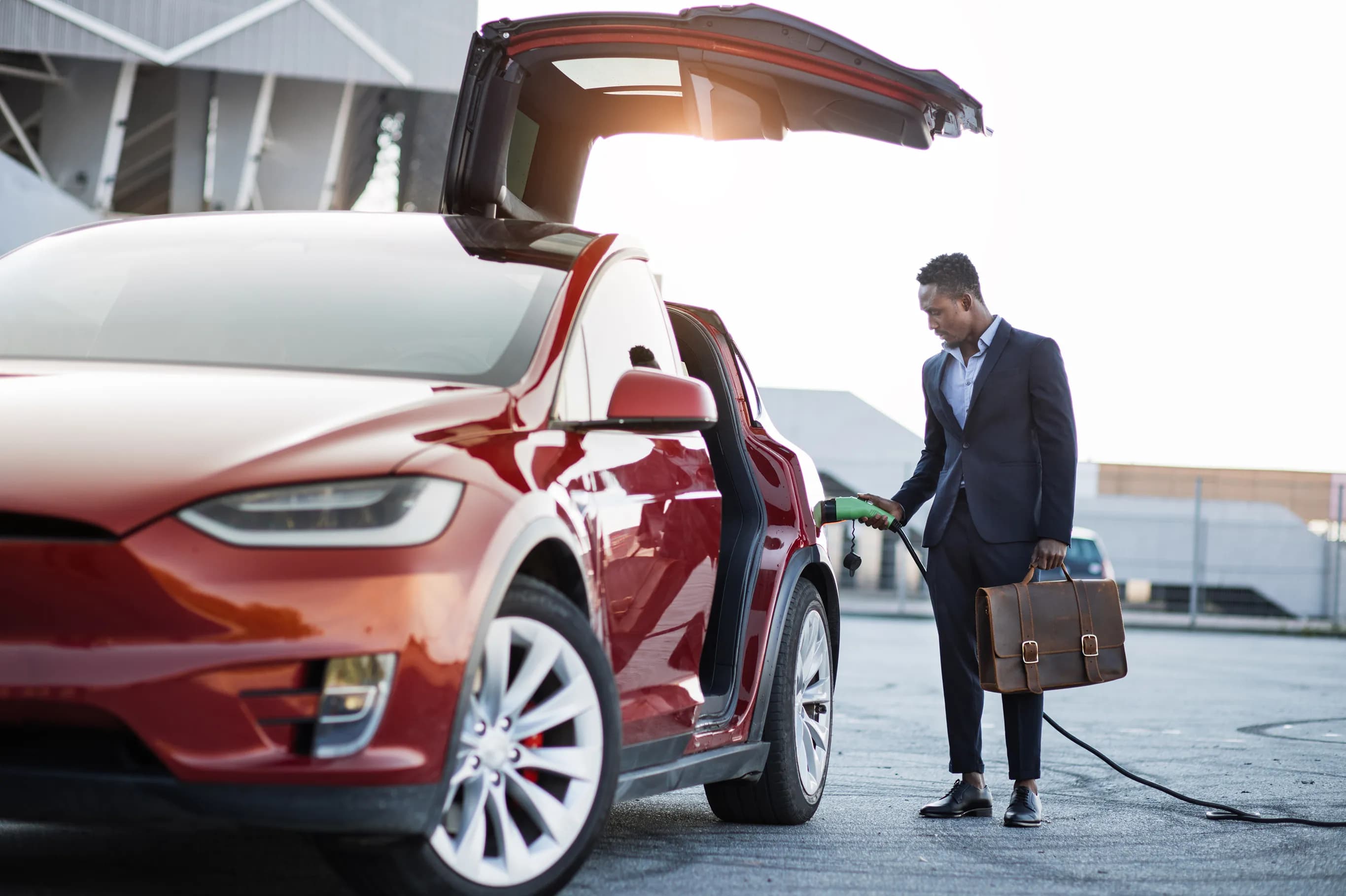 Business man with suitcase charging a red Tesla Model X.